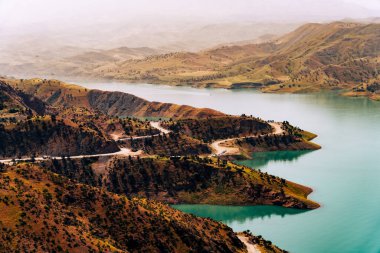 Dönemeç yolu göle çıkan bir dağ sırası. Yol ağaçlarla çevrili ve göl sakin ve mavi.