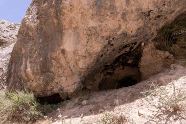 İçinde küçük bir mağara olan büyük bir kaya. Mağara karanlık ve kaya toprakla kaplı.