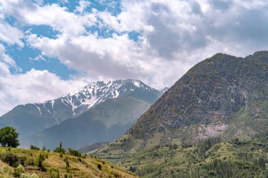Dağlar karla kaplı ve gökyüzü bulutlu. Dağlar çok yüksek ve onları kar kaplıyor.