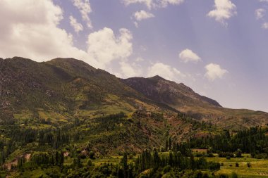 Dağlar yeşil ağaçlarla çevrili ve gökyüzü berrak.