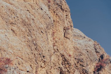 Arka planda mavi gökyüzü olan kayalık bir uçurum. Görüntü dengesiz ve engebeli.