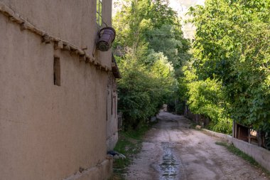 Yan tarafında bir ev olan toprak bir yol. Evin tavanında asılı bir sepet var.