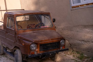 Eski kahverengi bir kamyon bir binanın önünde park edilmiş. Kamyon kirli ve soluk turuncu bir rengi var. Manzara nostaljik ve melankoliktir.