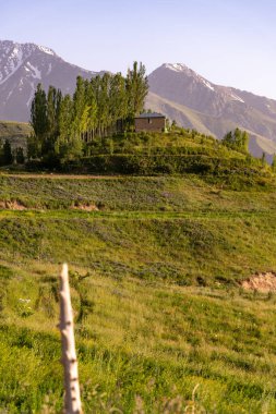 Tepesinde bir ev olan bir dağ sırası. Ev ağaçlarla çevrili ve manzara yemyeşil.