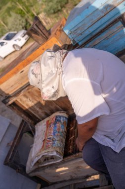 Bir adam tahta bir bankta oturuyor, kucağında bir torbayla. Poşette 