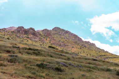 Açık mavi gökyüzü ve birkaç bulutu olan bir dağ sırası. Gökyüzü çok parlak ve güneş parlıyor.