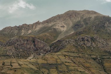 Dağ kayalarla kaplı ve kayalık, çorak bir görünüme sahip. Gökyüzü bulutlu ve dağ bir kar tabakasıyla kaplı.