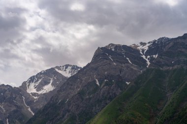 Dağlar karla kaplı ve gökyüzü bulutlu. Dağlar çok yüksek ve onları kar kaplıyor.