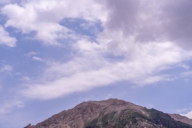 Arkasında bulutlu bir gökyüzü olan bir dağ. Gökyüzü mavi ve bulutlar beyaz