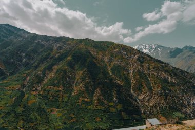 Bulutlu bir gökyüzü ve küçük bir kulübesi olan bir dağ sırası.