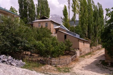 Önünde çit olan küçük bir ev. Ev ağaçlarla çevrili ve bir sürü yeşilliği var.