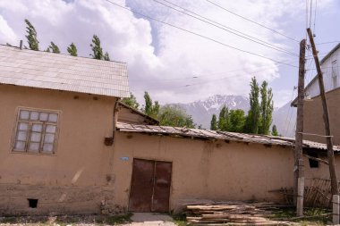 Kahverengi çatılı ve kapısında mavi işareti olan bir ev. Evin etrafı ağaçlarla çevrili ve arkasında bir dağ var.