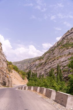 Arka planda dağ olan bir yol. Yol dar ve dolambaçlı. Gökyüzü açık ve mavi
