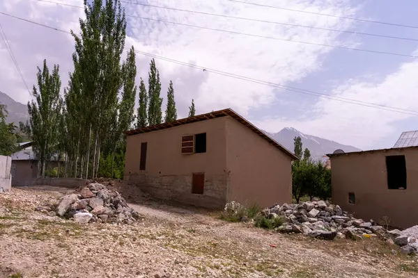 Arka planda birkaç ağaç ve kirli bir garaj yolu olan küçük bir ev. Evin etrafı kayalarla çevrili ve taş bir duvarı var.