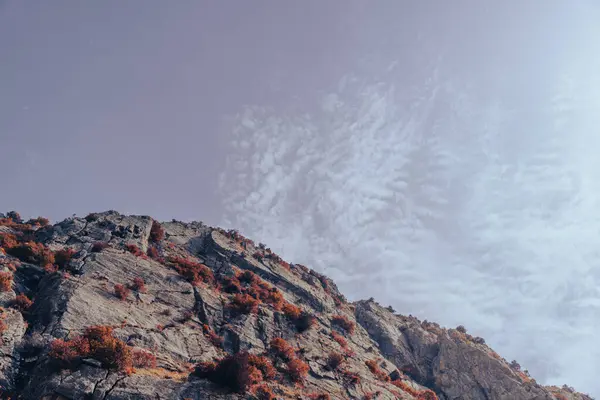 Arkasında bulutlu bir gökyüzü olan bir dağ. Gökyüzü çoğunlukla mavi ve bulutlar etrafa saçılmış.