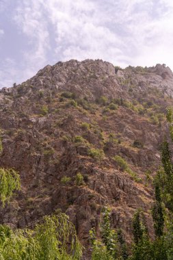 Kayalık, çorak yamaçlı bir dağ. Gökyüzü bulutlu ve güneş parlıyor