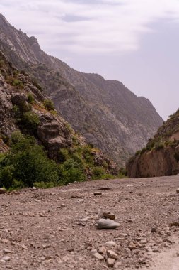 Aralarında toprak yol olan kayalık bir dağ sırası. Yol boş ve gökyüzü bulutlu.