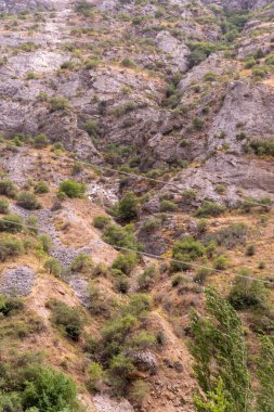 Birkaç ağaç ve içinden bir kablo geçen kayalık bir dağ. Kablo bir elektrik hattına bağlı.