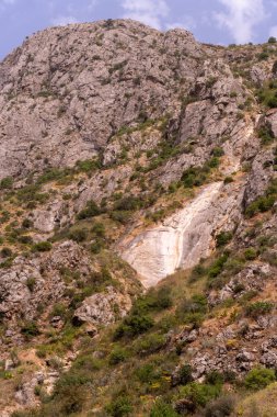 Uçurumu ve şelalesi olan bir dağ. Dağ ağaçlar ve kayalarla kaplı.