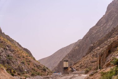 Ortasında toprak bir yol ve büyük bir beton bina olan bir dağ sırası. Gökyüzü açık ve güneş parlıyor.