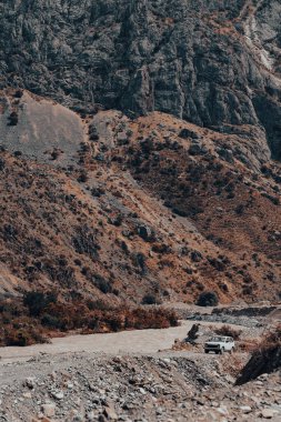 Bir araba dağlarda toprak bir yolda ilerliyor.