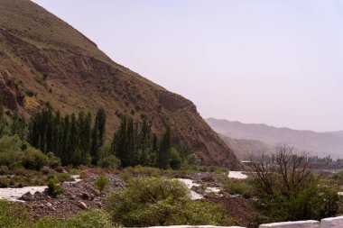 İçinden nehir akan bir dağ sırası. Gökyüzü bulutlu ve güneş görünmüyor.
