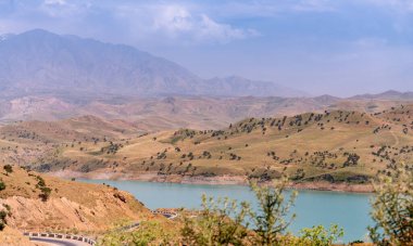 Önünde göl olan güzel bir dağ sırası. Gökyüzü açık ve güneş parlıyor.