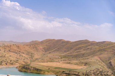 Önünde göl olan bir dağ sırası. Gökyüzü açık ve güneş parlıyor.