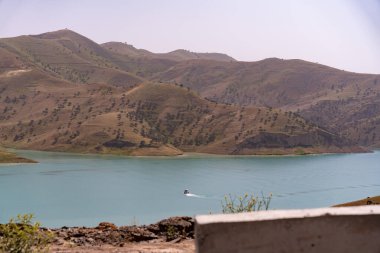 Bir dağın önündeki gölde bir tekne yüzüyor. Göl sakin ve gökyüzü temiz.