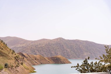 Önünde göl olan bir dağ sırası. Gökyüzü açık, dağlar ise ağaçlarla çevrili.