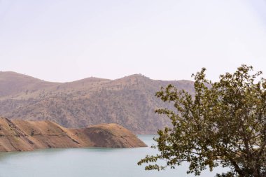 Önünde göl olan bir dağ sırası. Gökyüzü açık ve güneş parlıyor.