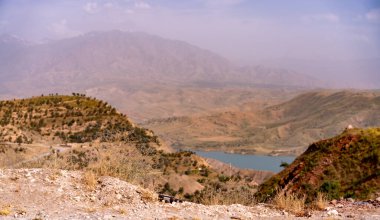 Uzakta gölü olan bir dağ sırası. Gökyüzü bulutlu ve dağlar ağaçlarla kaplı.