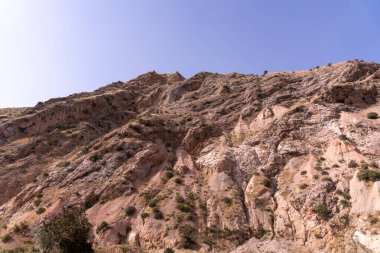 Arka planda açık mavi gökyüzü olan kayalık bir dağ. Dağ kayalarla kaplı ve seyrek bir bitki örtüsü var. Gökyüzü parlak ve berrak, ortama huzurlu ve huzurlu bir atmosfer veriyor.