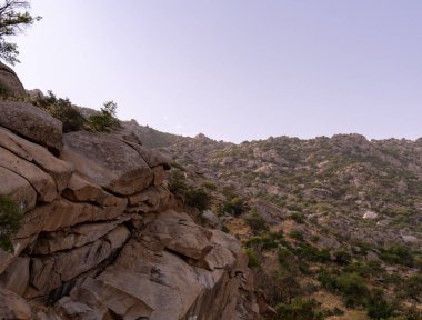 Arka planda açık mavi gökyüzü olan kayalık bir yamaç. Gökyüzü bulutlarla dolu, ortama huzurlu ve huzurlu bir atmosfer veriyor.