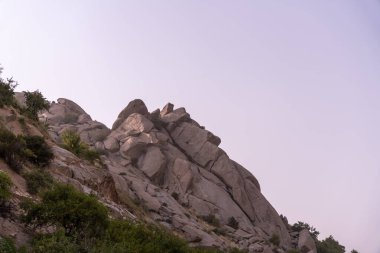 Arkasında bulutlu bir gökyüzü olan kayalık bir dağ. Gökyüzü mavi ve beyazın bir karışımıdır. Görüntüye huzurlu ve huzurlu bir atmosfer verir.
