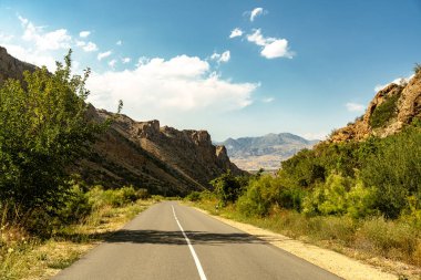 Arka planda dağ olan bir yol. Yol boş ve gökyüzü mavi.
