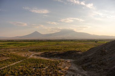 Uzakta açık mavi gökyüzü ile bir dağ sırası görülebilir. Dağlar ağaçlarla örtülmüş, gökyüzü bulutlarla doludur. Huzurlu ve huzurlu bir sahne.