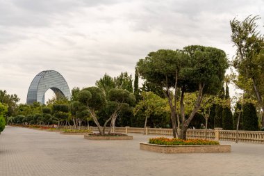 Arkasında büyük bir bina olan bir park. Ağaçlar yeşil, çiçekler turuncu.