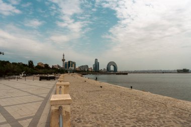 Arkasında şehir olan bir sahil. Kumsal boş ve gökyüzü bulutlu. Şehir uzakta ve su sakin.