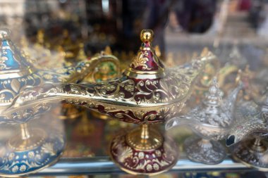 Altın ve kırmızı cam lambaların bir koleksiyonu cam bir kabın içinde sergilenir. Lambalar çeşitli şekil ve boyutlarda ve hepsinin üzerinde karmaşık tasarımlar var. Sahne zarifliktir.