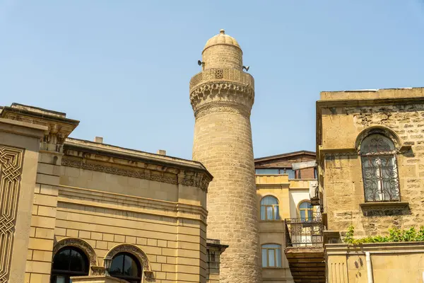 Üzerinde kule ve saat olan yüksek bir bina. Binanın etrafı başka binalarla çevrili ve bir sürü penceresi var.