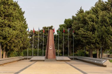 Üzerinde bayraklar olan büyük bir anıt. Bayraklar farklı renk ve boyutlarda. Anıt ağaçlar ve bir patikayla çevrili.