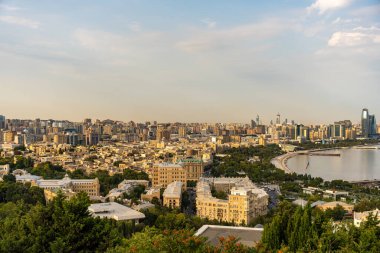 Arka planda büyük bir su kütlesi olan bir şehir manzarası. Şehir yüksek binalarla dolu ve gökyüzü açık.