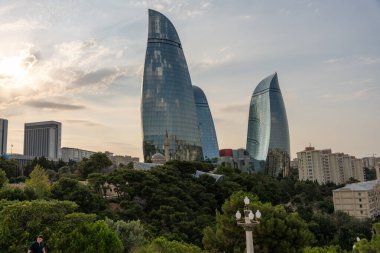 Önünde iki yüksek bina ve bir park olan bir şehir silueti. Gökyüzü bulutlu ve güneş batıyor.