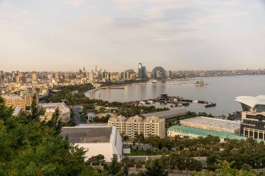 Arka planda büyük bir su kütlesi olan bir şehir manzarası. Şehir yüksek binalarla dolu ve su sakin.