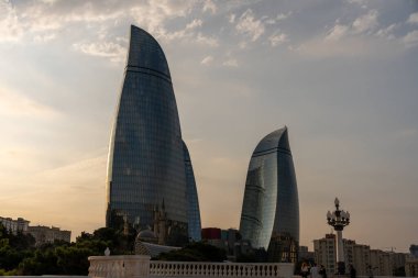 Arka planda bulutlu bir gökyüzü ve bir sürü penceresi olan iki uzun bina. Binalar çok yüksek ve eşsiz bir şekli var.