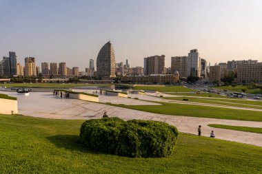 Arkasında büyük bir bina olan bir şehir parkı. Gökyüzü mavi ve güneş parlıyor.