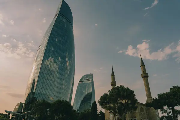 İki büyük binası ve büyük bir camisi olan bir şehir silueti. Gökyüzü açık ve güneş batıyor.