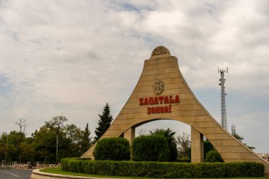 Üzerinde Zadatala yazan büyük bir kemer yolu. Kemer yolu çalılar ve ağaçlarla çevrili.