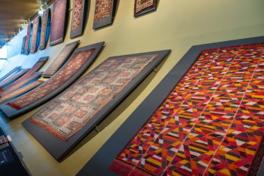 Değişik desenleri ve tasarımları olan renkli halılardan oluşan bir duvar. Duvar ahşaptan yapılmış ve halılar duvardan sarkıyor.